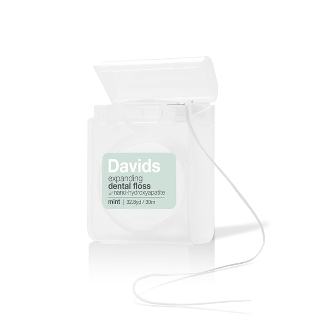 A clear container of Davids Expanding Dental Floss with Hydroxyapatite and a mint flavor. The lid is open, showing floss pulled from its innovative refill system, with packaging highlighting 32.8 yards (30 meters) of premium care.