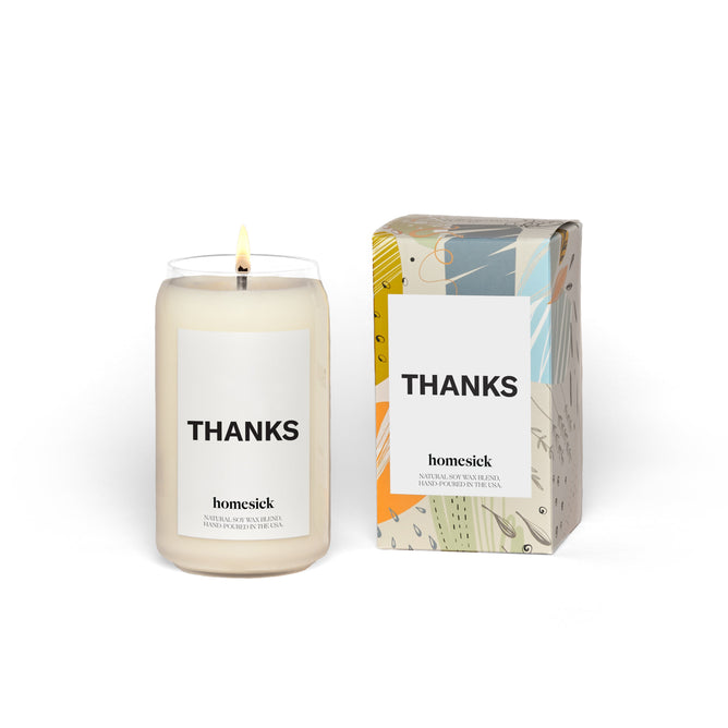 The Homesick Thanks Candle, made from natural soy wax with Ylang Ylang and White Musk notes, stands lit in a glass jar labeled THANKS beside its colorful box, showcasing the brand’s signature personalized packaging. This cruelty-free candle embodies gratitude seamlessly.