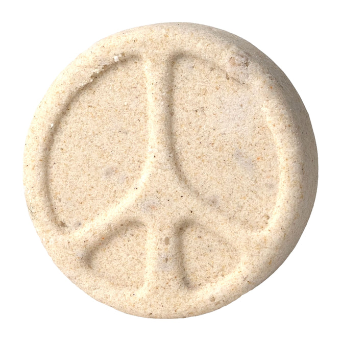 The Dirty Hippie Froth Bomb by Pacha Soap Co. is a round, oatmeal-hued tablet with a textured surface and an engraved raised peace symbol.