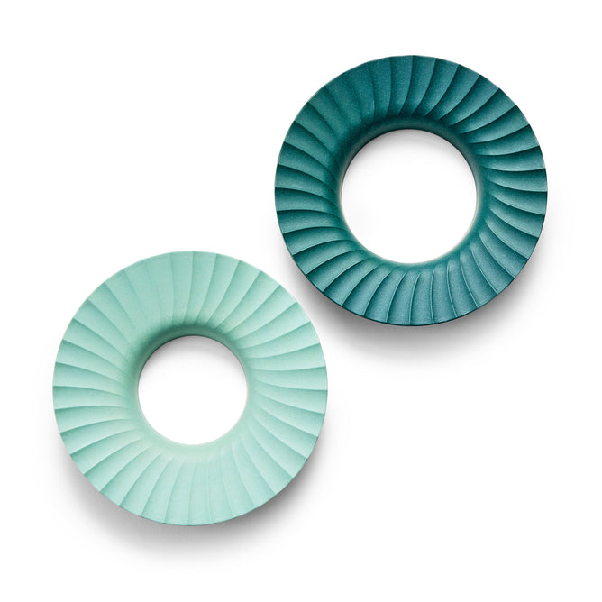 Modern Sprouts Produce Keepers, crafted from renewable materials, feature two circular objects with spiral grooves against a white background. One is light green, the other dark teal. They have hollow centers and are arranged diagonally with the dark teal in the upper right.