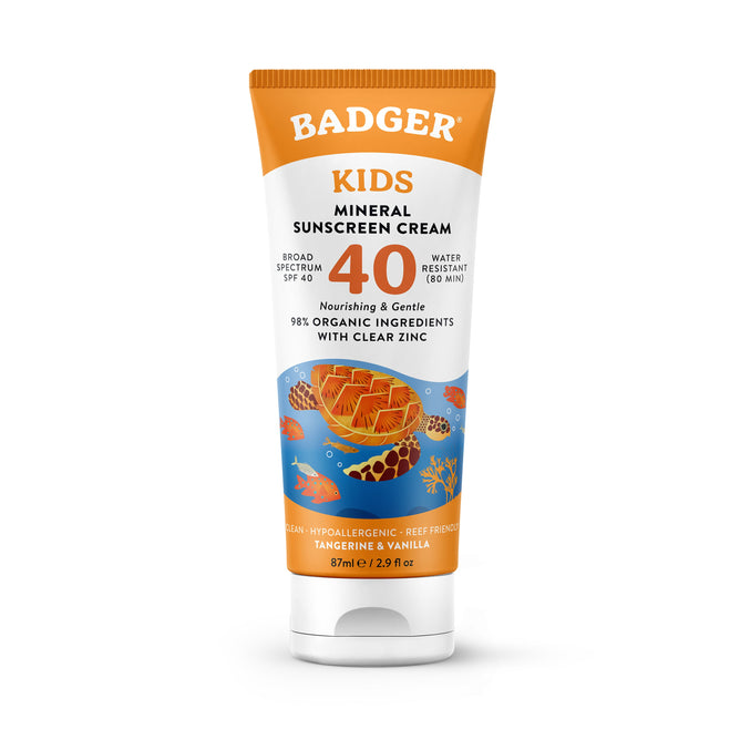Badger Balms Kids Mineral Sunscreen Cream - SPF 40, crafted for sensitive skin, includes an orange cap and ocean-themed design. This organic lotion boasts a tangerine-vanilla scent with water-resistant clear zinc protection.
