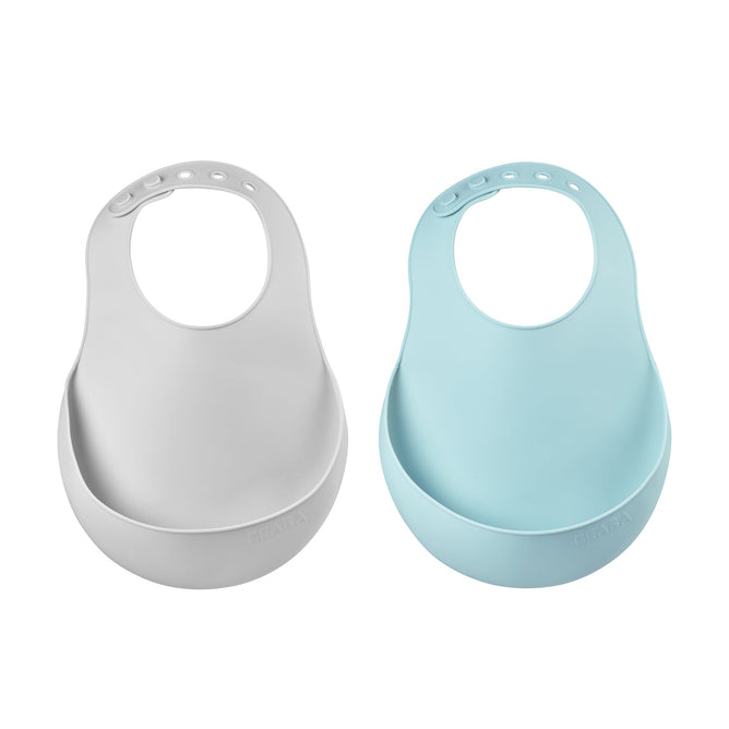 Displayed side by side are two BEABA Silicone Bibs, a must-have for feeding. In light gray and light blue, they feature snap closures and large front pockets to catch spills. Dishwasher safe for easy cleaning.