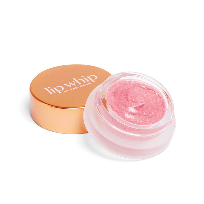 Open the Lip Whip Color Balm by Kari Gran, featuring a pink hue with subtle shimmer. This natural lip balm is packaged in a small round glass jar, accompanied by a gold-colored lid.