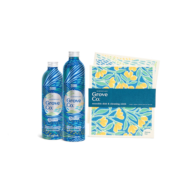 Two decorative blue bottles labeled Grove Collaborative, with the limited edition Atlantic Dune Grass scent, sit beside yellow floral-patterned reusable dish and cleaning cloths, all from the Scented Trio - Spring Collection, set against a pristine white background.