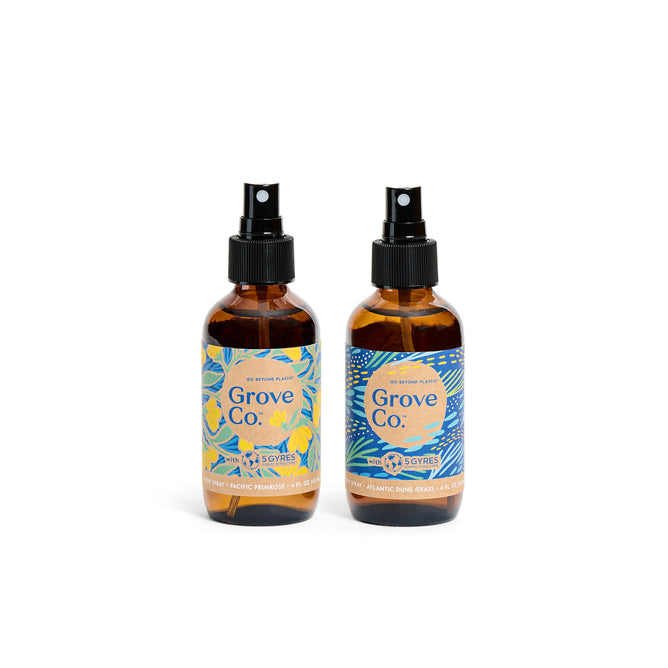 The Room Spray Set - Spring Collection by Grove Collaborative includes two dark amber glass bottles with black nozzles and vibrant labels. One features a citrus design, while the other is inspired by Atlantic Dune Grass, both part of the limited edition spring collection.