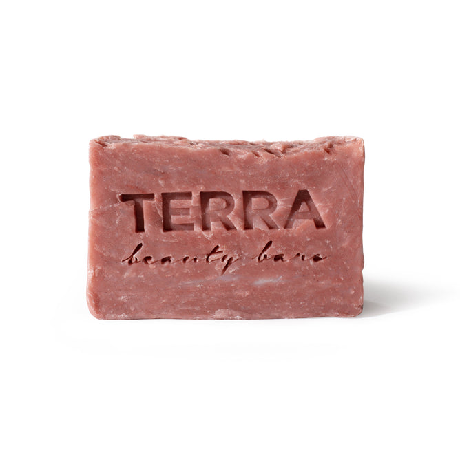 A Naked Rose Facial Beauty Bar by Terra Beauty Bars, engraved with the brand name, gracefully sits against a white background. Its pinkish-red color and slightly rough rectangular form are crafted from natural ingredients, merging elegance with natures purity.