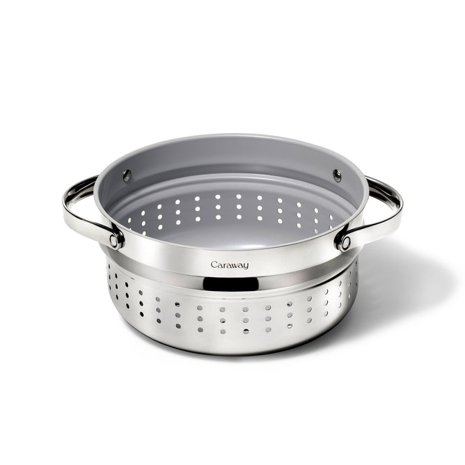 The Caraway Stainless Steel Dutch Oven Steamer, 6.5 qt, features a non-toxic design with two handles and a perforated pattern. It has a sleek look on a plain white background with the brand name prominently displayed on the side.