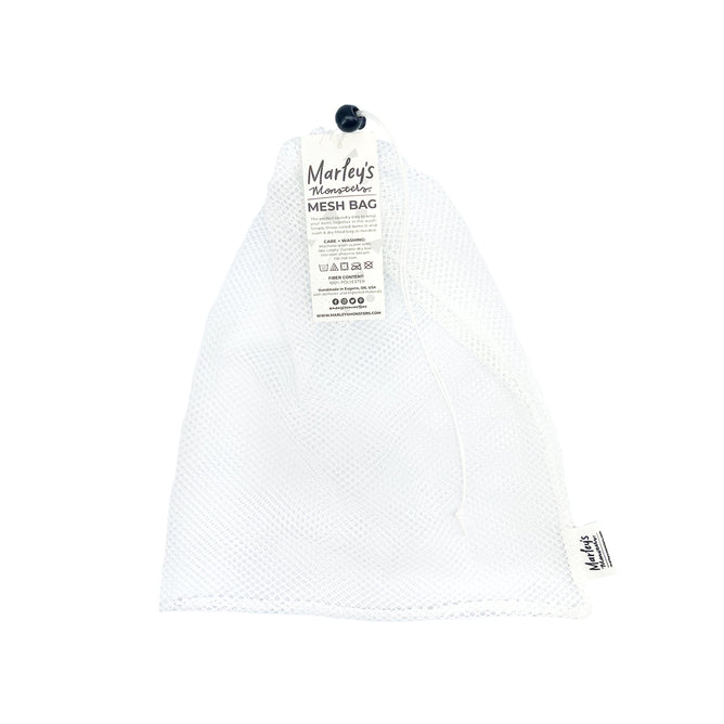 The Mesh Laundry Bag by Marleys Monsters is a white mesh bag with a drawstring closure and black toggle. It includes a tag with product info, icons, and branding. This lightweight, reusable design is ideal for storing UNpaper Towels or serving as a chic laundry bag.