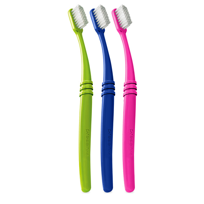 Displayed side by side are three Preserve toothbrushes (Soft): green, blue, and pink. Each recyclable brush flaunts a white bristle head and a curved handle embossed with the brand name, crafted from recycled plastic to ensure sustainability and style.