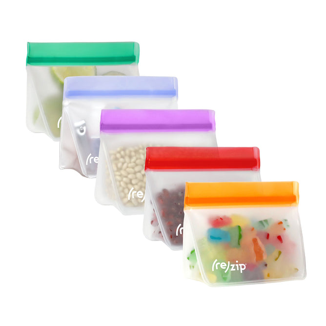Five (re)zip Stand-Up Snack - 1 Cup Bags are lined up, each sealed with a zip in green, blue, purple, red, or orange. These airtight storage bags contain items like sliced limes, white beans, red beans, and colorful candies.