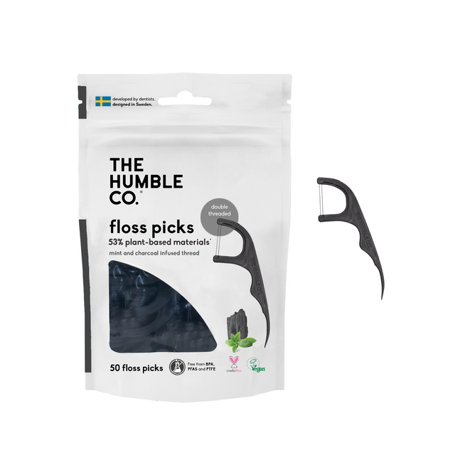 A pack of The Humble Co. Dental Floss Picks sits beside a single floss pick, featuring its 53% plant-based, cruelty-free materials. The mint and charcoal-infused thread ensures freshness and effectiveness. Each pack includes 50 expertly crafted picks for a healthier smile.
