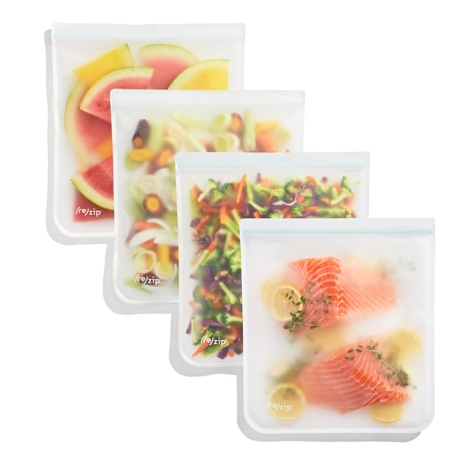 Four transparent, BPA-free (re)zip Flat Gallon Bags are lined up, each holding sliced watermelon, mixed vegetables, mixed salad, or raw salmon with lemon slices and herbs. These leak-proof bags have a zip closure for added convenience.