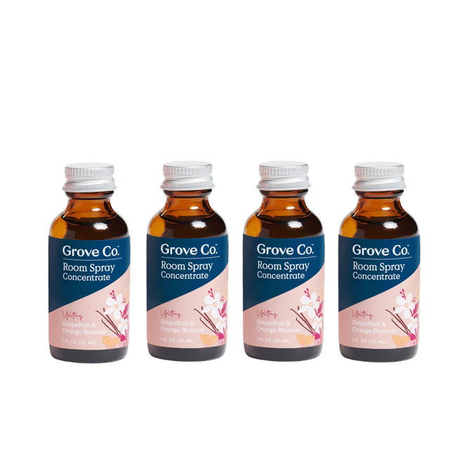 Four Grove Co. Room Spray Refill Gift Set bottles are lined up, each with a brown glass body and a vibrant label featuring cherry blossoms, highlighting natural fragrance and recyclable packaging. The label reads Grove Co. Room Spray Concentrate.