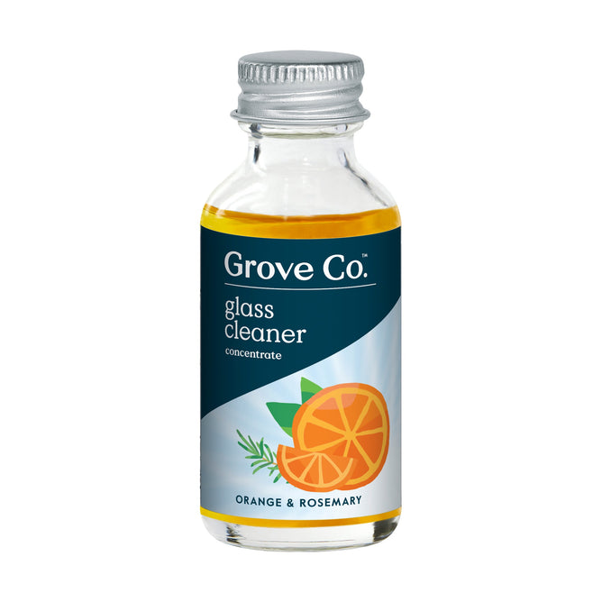 Grove Co.s Glass Cleaner Concentrate comes in a small clear bottle with a metal cap and features a label with an orange slice, rosemary sprig, and Orange & Rosemary text. The plant-based liquid inside is light yellow-orange, emitting a natural fragrance.
