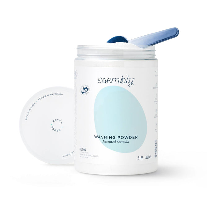 A container of Esembly Babys all-natural Washing Powder with the lid off, showing a scoop inside. The white container features a large pastel blue oval highlighting its eco-friendly packaging and patented formula, ideal for sustainable cloth diaper care.