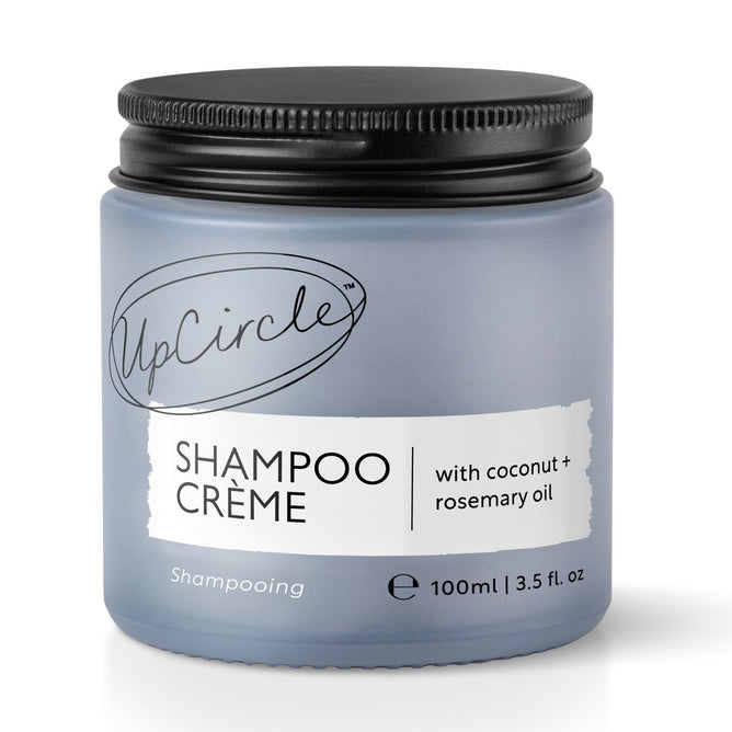 The UpCircle Shampoo Crème, in a 100ml blue-gray jar with a black screw-on lid, uses coconut and grapefruit oil to revolutionize hair care. Its minimalist design underscores the natural ingredients of this hybrid shampoo crème.