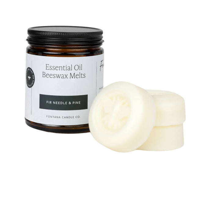 An open jar labeled Essential Oil Beeswax Melts - Fir Needle and Pine from Fontana Candle Co. has three cream-colored wax melts stacked beside it. Made with pine needle essential oils, it sits on a dark jar with a white label and is MADE SAFE® certified for peace of mind.