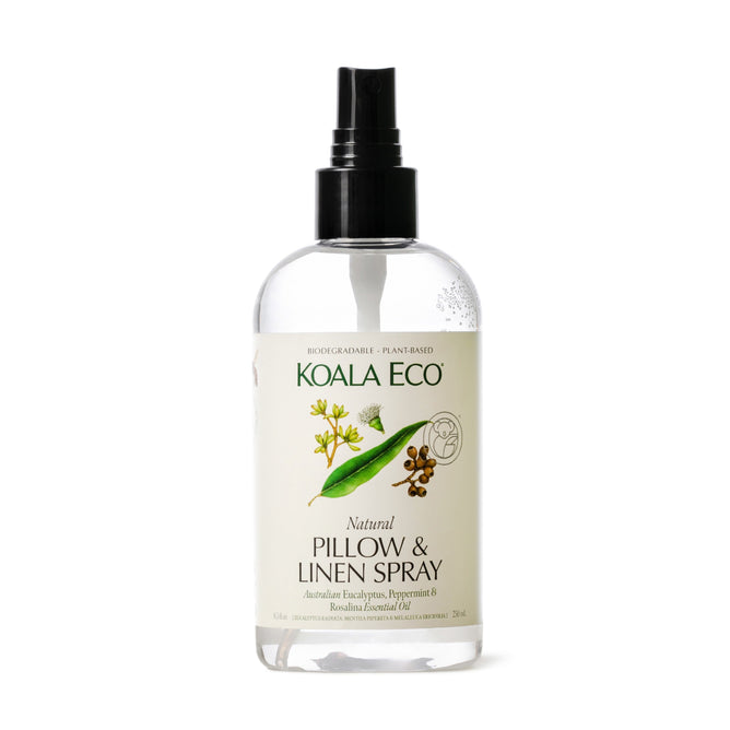 A transparent 7 fl oz spray bottle from Koala Eco is labeled Natural Pillow & Linen Spray and features a design with green leaves and brown pods. Its made with an eucalyptus, peppermint, and rosalina blend of Australian essential oils.