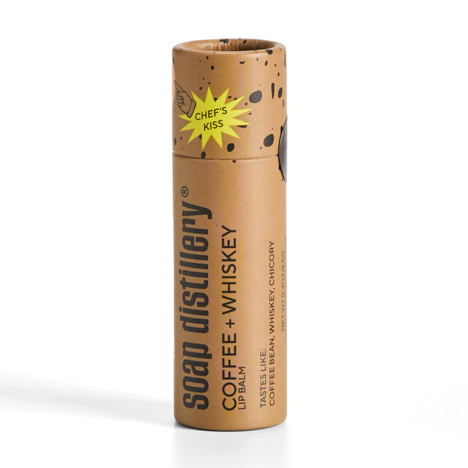 Soap Distillerys Lip Balm comes in a speckled brown cardboard tube and features bold flavors of coffee bean, whiskey, and chicory. The Chefs Kiss starburst icon promises a captivating sensory delight.
