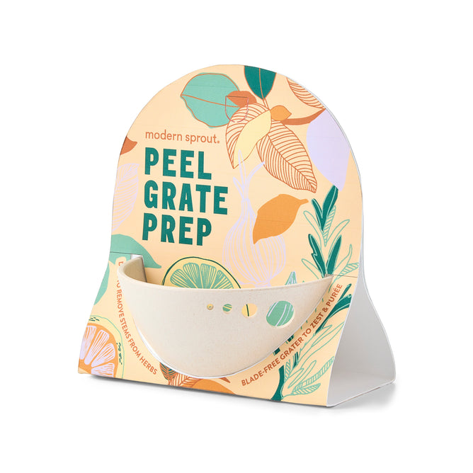 The packaging of the Peel, Grate & Prep Dish by Modern Sprout showcases vibrant illustrated leaves and citrus slices. It reads: modern sprout \npeel grate prep \nblade-free integrated grater zest and pare, featuring versatile culinary functions with a small bowl attached at the bottom.