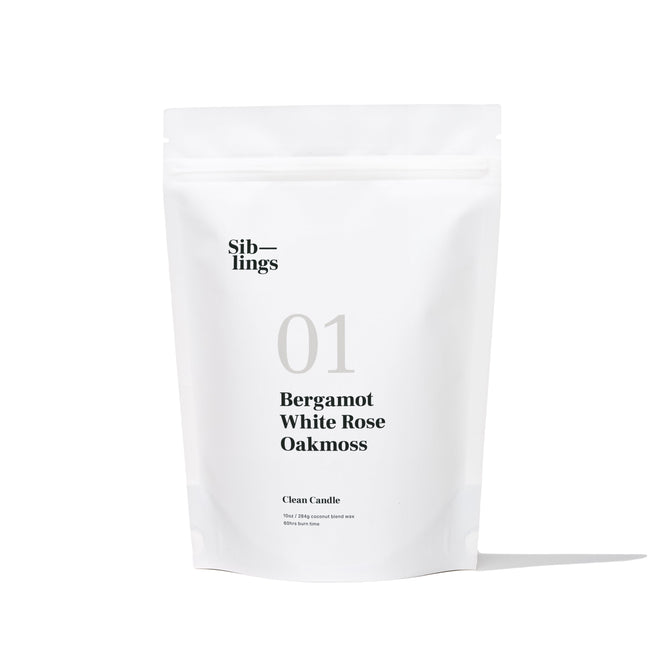 A white Siblings 01 packet labeled as a DIY Candle Kit displays Bergamot, White Rose, Oakmoss. Its described as a Clean Candle with compostable packaging and clean ingredients, weighing 210g. Positioned upright against a white backdrop, it casts a slight shadow.