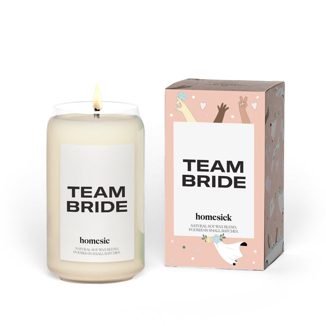 A white Team Bride candle in a glass jar from Homesick, made from a natural soy wax blend, complements a decorative box with the same text. Perfect for bridal parties, it evokes the joy of sparkling rosé celebrations.