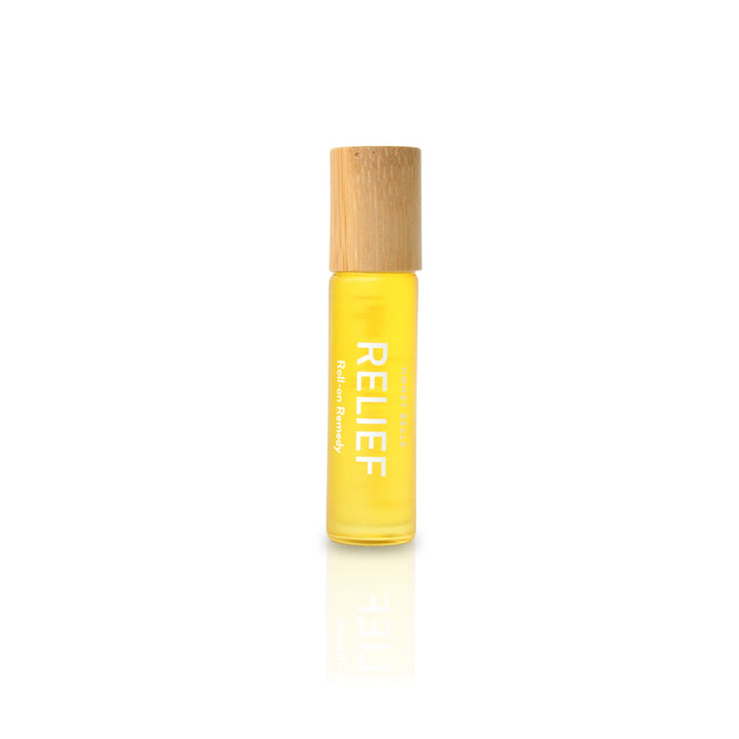 A yellow Honey Belle roll-on bottle labeled RELIEF, featuring Roll-on Remedy, infused with essential oils for a soothing aromatherapy experience. The bottle stands upright on a reflective white surface, capped with light wood.