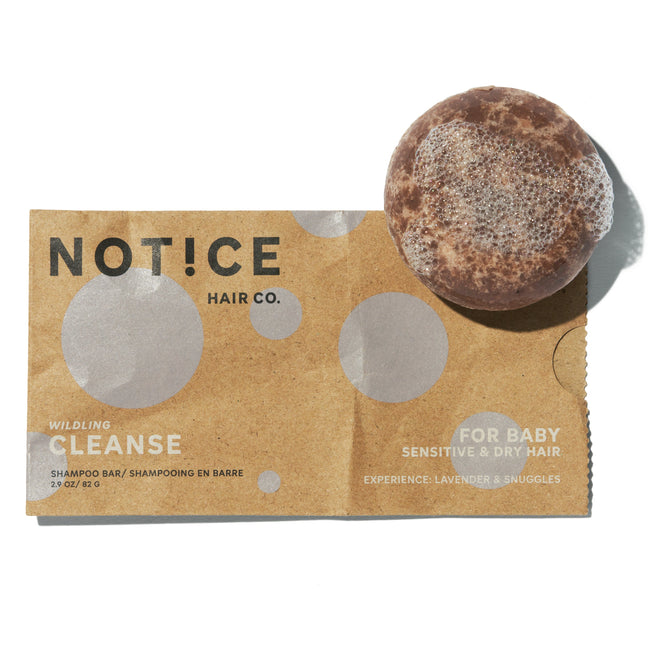 NOT!CE Hair Co’s Cleanse Baby Shampoo Bar comes in a round shape with brown paper packaging labeled WILDling CLEANSE and FOR BABY, SENSITIVE & DRY HAIR. It features a lavender and snuggles scent and is infused with moisturizing aloe vera, ideal for sensitive skin.