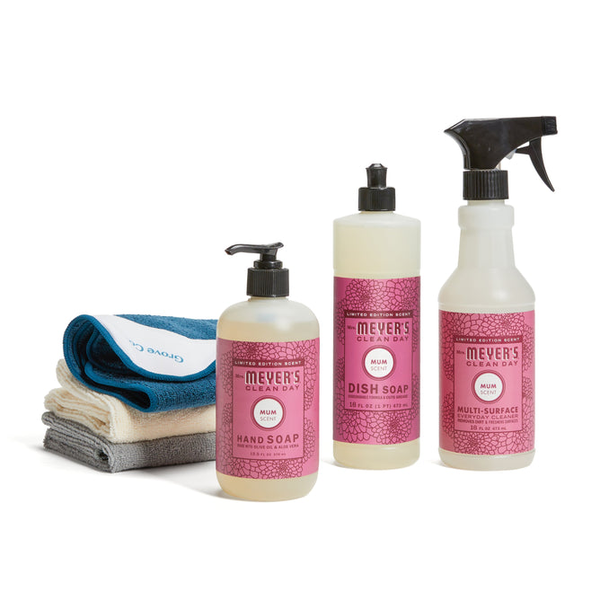 Three bottles from the Mrs. Meyers fall-cleaning-set-mmcd—hand soap, dish soap, and multi-surface spray—are shown beside a neatly stacked trio of folded cleaning cloths.