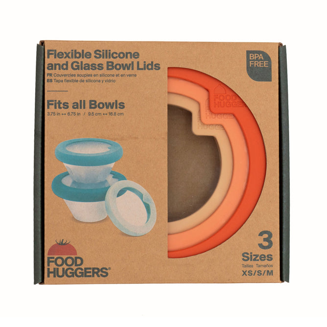 Food Huggers Flexible Silicone and Glass Bowl Lids feature an airtight seal and are BPA-free. The packaging highlights the transparent glass centers of the orange and peach lids, available in three sizes to fit any bowl perfectly.