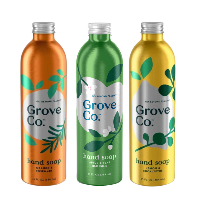 Three sleek metallic bottles from the Grove Collaborative Refillable Fruit Hydrating Hand Soap Set feature vivid orange, green, and yellow hues. The labels display scents like Orange & Rosemary, Apple & Pear Blossom, and Lemon & Eucalyptus with elegant leaf designs.