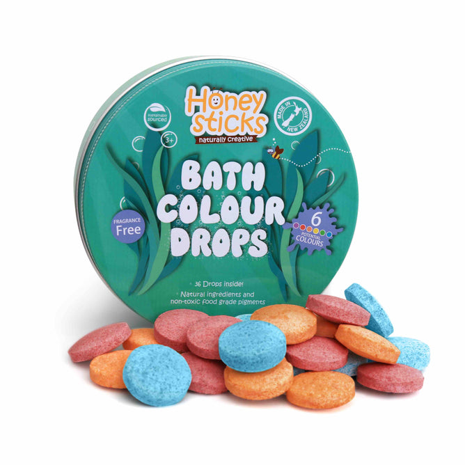A round tin labeled Honeysticks Bath Drops features scattered blue, orange, and pink drops. This fragrance-free addition to your bath routine offers 36 vibrant Honeysticks Bath Drops made with natural ingredients.