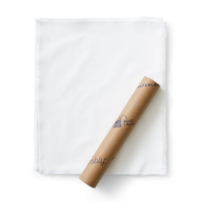 A brown cardboard roll with blue text and a pattern rests diagonally on folded Esembly Baby Reusable Paper Towels made of certified 100% unbleached Organic Cotton, all set against a plain white background.