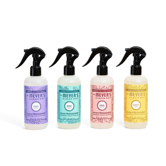 The Spring Room Freshener Collection by Mrs. Meyers includes four bottles in Lilac (purple), Mint (green), Rose (pink), and Daisy (yellow) scents, each topped with a sleek black spray nozzle for elegance.