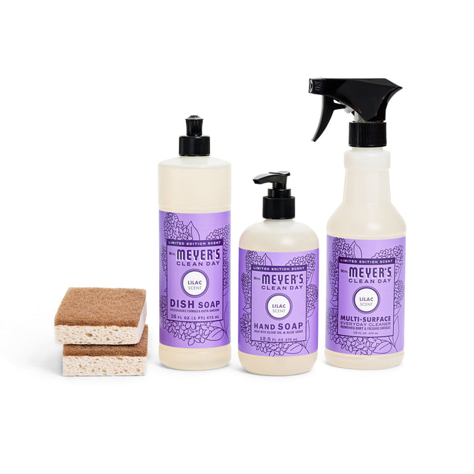 The Blooming Buds Scrubbing Set features three Mrs. Meyers Clean Day lilac-scented products—dish soap, hand soap, and multi-surface cleaner—with two walnut scrubber sponges against a white background.