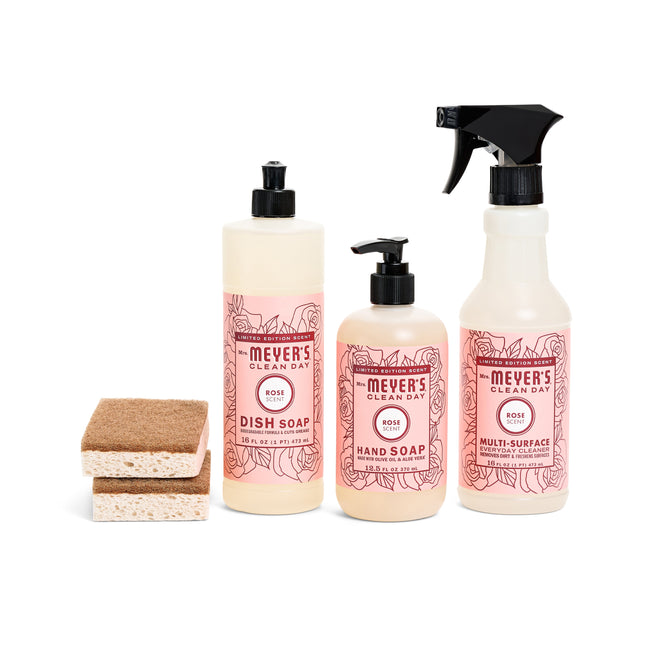 Displayed are four cleaning products: two sponges from the Blooming Buds Scrubbing Set and three containers from Mrs. Meyers, including dish soap, hand soap, and multi-surface cleaner—all rose-scented with pink labels and a blooming buds design.
