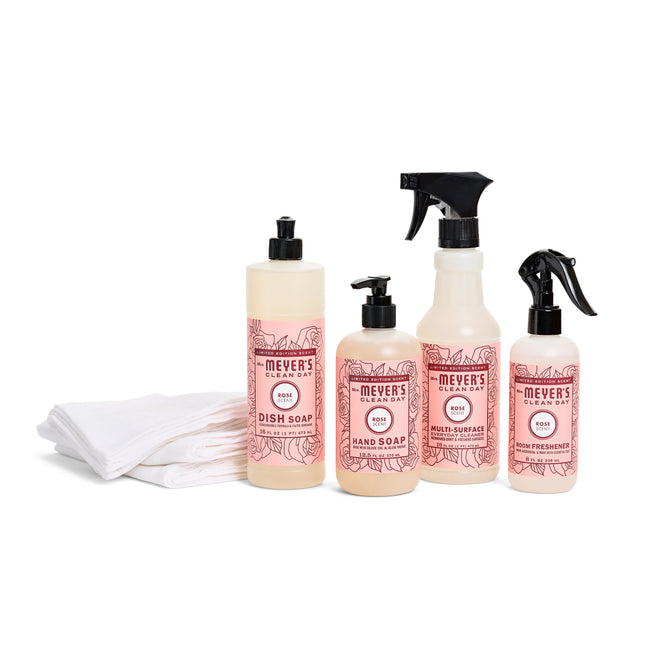 Explore the Sinkside Spring Cleaning Set by Mrs. Meyers, featuring rose-scented dish soap, hand soap, multi-surface cleaner, and air freshener. Paired with an organic cotton towel on a pristine white background, they offer eco-friendly freshness for your home.