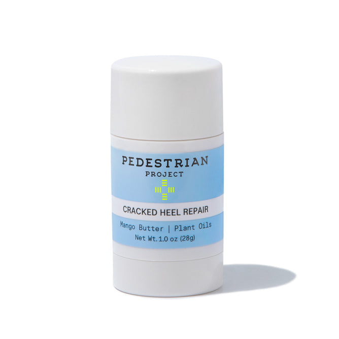 Pedestrian Projects Cracked Heel Repair balm comes in a cylindrical stick container with a blue label listing Mango Butter and Plant Oils. Weighing 1.0 oz (28g), it provides dry skin relief and prevents blisters, casting a soft shadow on a light background.
