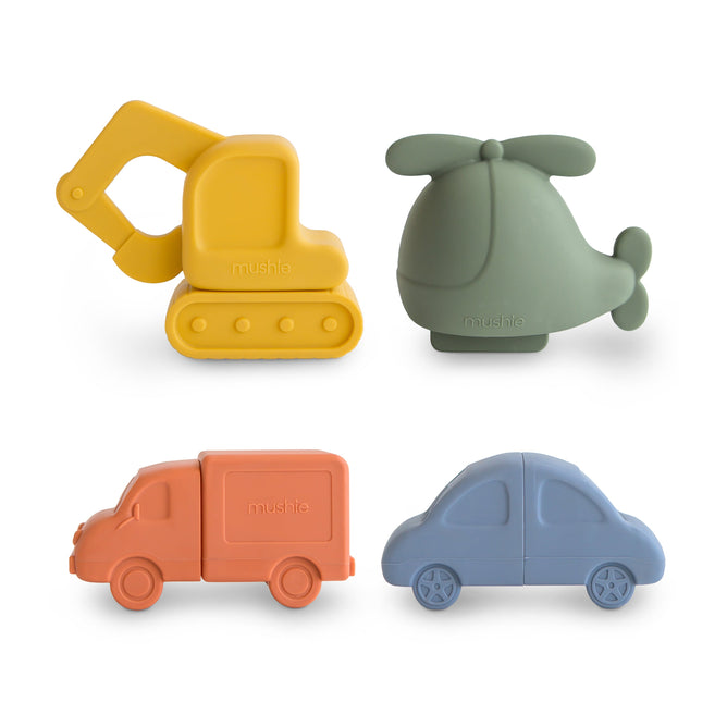 The mushie Vehicles Mold-Free Bath Toy Set – Soft Silicone includes a yellow excavator, green helicopter, orange delivery truck, and blue car made from food-grade silicone. Dishwasher safe and shown on a white background.