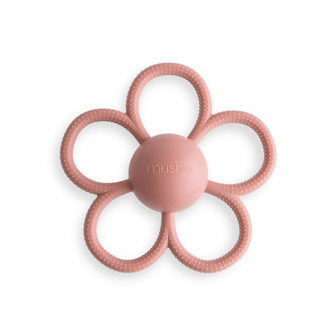 The mushie Daisy Rattle Teether is a pink, flower-shaped baby teether with six textured loops and a smooth round center embossed with mushie. Made from BPA-free, food-grade silicone. Shown on a white background.