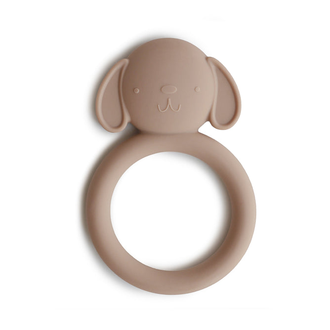 The mushie Dog Soothing Teether is a beige, circular baby teether with a cute dog face and floppy ears, made from BPA-free, food-grade silicone. Safe and non-toxic, it is shown on a white background.