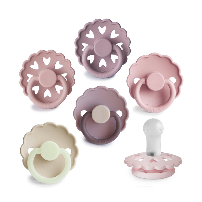 Six mushie FRIGG Natural Rubber Pacifiers (BPA-free, for 0-6 months) in soft pastels are arranged on a white background. Five show the front and one the side, highlighting scalloped edges and heart-shaped cutouts. Made in Denmark.