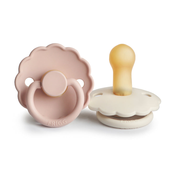 Two mushie FRIGG Daisy Natural Rubber Pacifiers (BPA-free, 6-18 months)—one light pink flat, one cream with yellow nipple upright—feature soft pastels and charming Danish design.