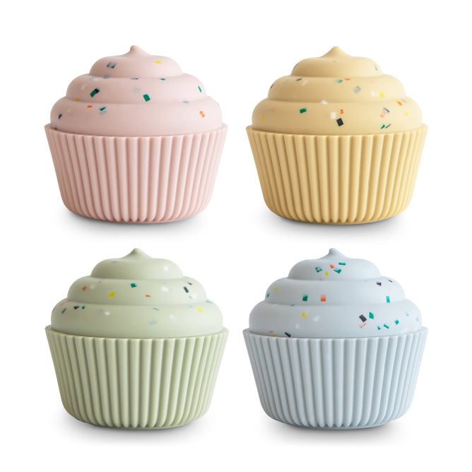 Four pastel cupcakes—pink, yellow, light green, and light blue—with swirled frosting sit in ribbed food-grade silicone wrappers. The mushie Mix & Match Cupcake Toy offers sensory play and is arranged in a two-by-two grid on a white background.