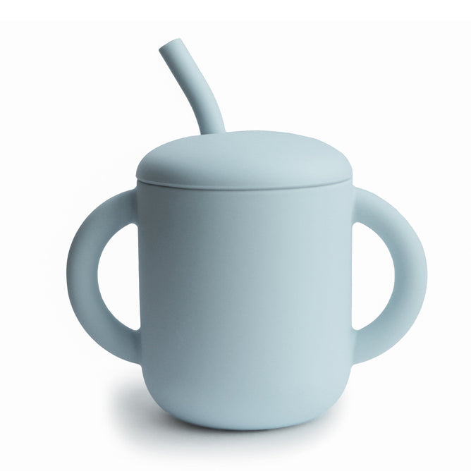 The mushie Silicone Training Cup with Straw is BPA-free, made from food-grade silicone in light blue, and features two large handles plus a lid with a short angled straw—perfect for your baby essentials. Shown on a white background.