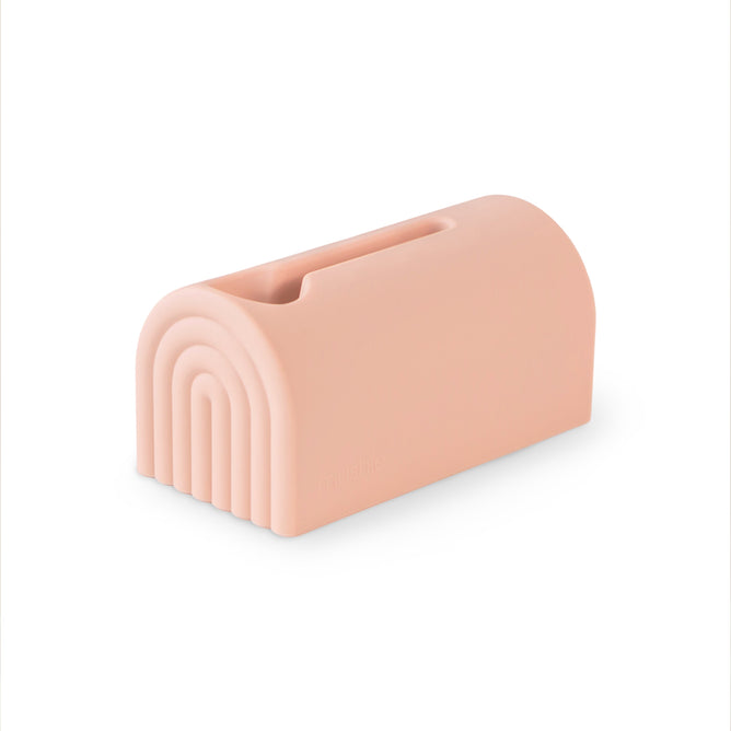 The mushie Bath Spout Cover – Soft Silicone is a rectangular, soft pink cover with rounded edges, a top slot, and a rainbow arch design on one end, offering bath time safety in style.