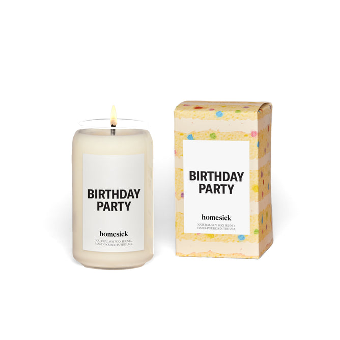 A lit Homesick Birthday Party Candle of natural soy wax sits beside colorful packaging reminiscent of a vanilla cake with confetti.