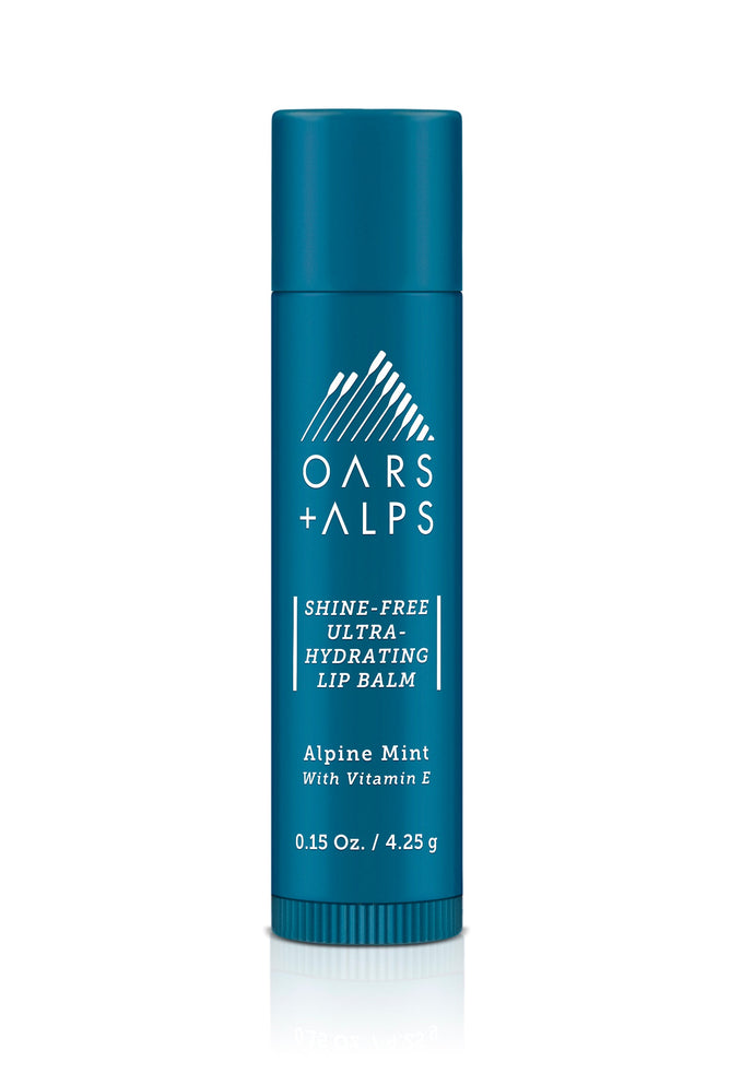 Oars + Alps Shine-Free Lip Balm comes in a blue cylindrical tube with white text. It features an alpine peppermint flavor, is enriched with Vitamin E, and is made from organic ingredients. The tube includes a mountain logo on top.