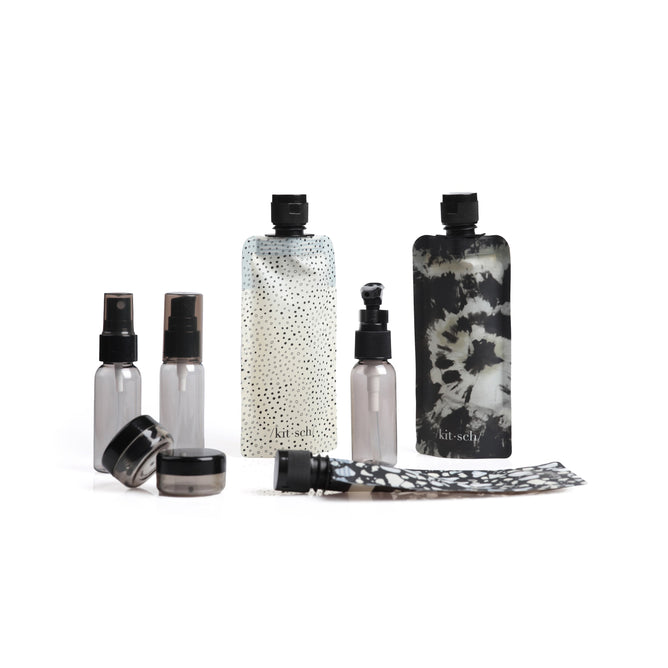 The Kitsch Travel Bottle Set features travel-sized, eco-friendly containers including spray bottles, jars, and pouches with chic black and white designs—polka dots and tie-dye. All items comply with TSA carry-on regulations.
