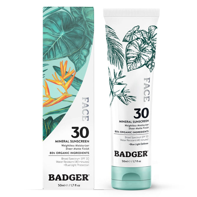 A tube of Badger Balms Face Mineral Sunscreen - SPF 30 is alongside its box featuring botanical designs with tropical leaves in green and orange. It provides SPF 30, mineral protection, shields against blue light, and contains 80% organic ingredients.
